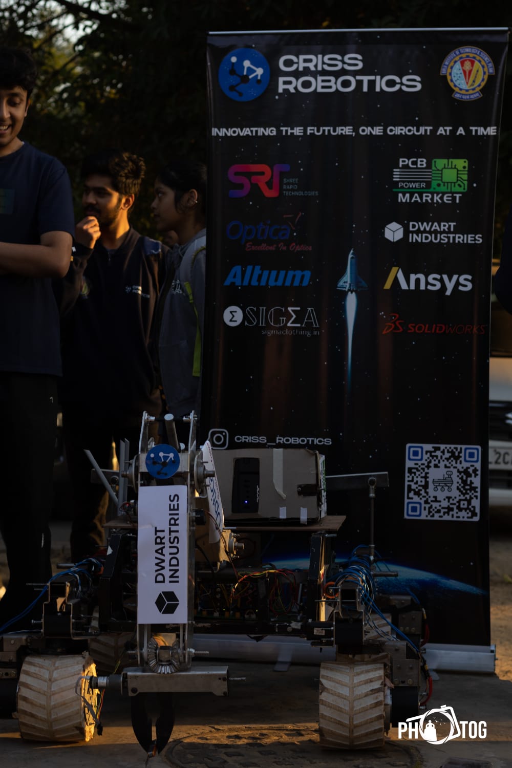 CRISS Robotics Mars rover on sandy competition terrain with Dwart Industries sponsor banner in background
